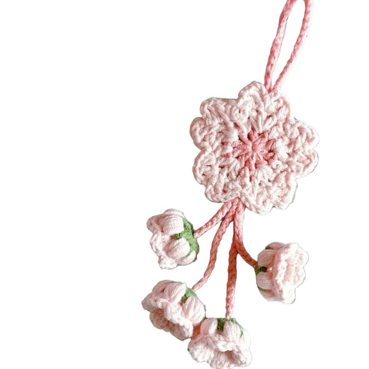Pink crocheted flower ornament on a gray surface with yarn and a book in the background.