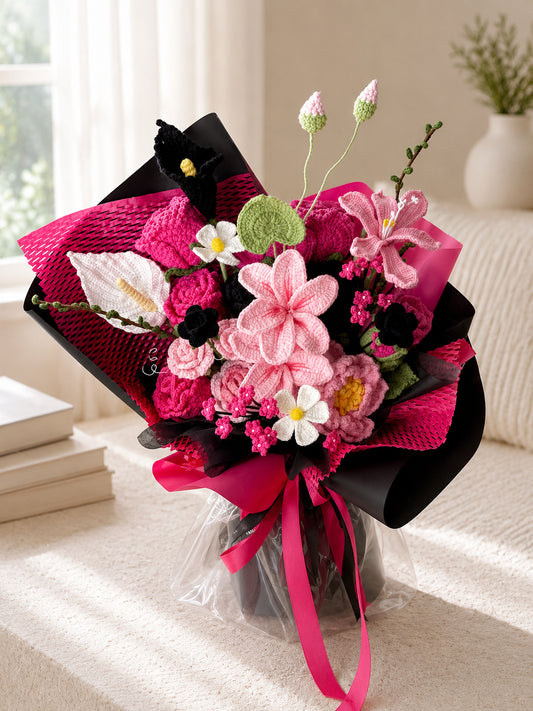 A handmade crochet flower bouquet in shades of pink, white, and black, wrapped in textured hot pink and black paper with a bright pink ribbon, displayed on a beige sofa.