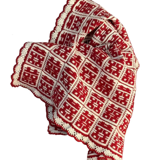 Red and white patterned fabric held by a person in a room with red cushions and a beige sofa.