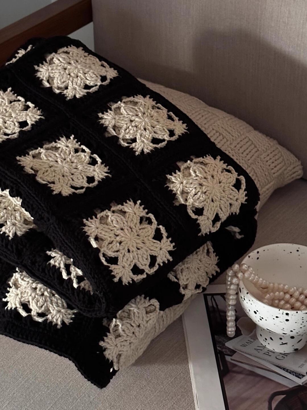 Black and white crocheted blanket on a chair with a bowl and books in the background.