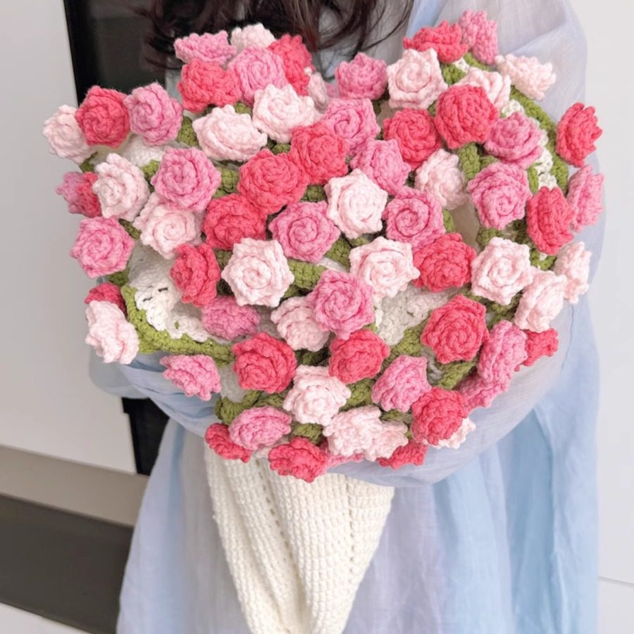 Heart-shaped bouquet made of pink and white crocheted flowers held by a person.