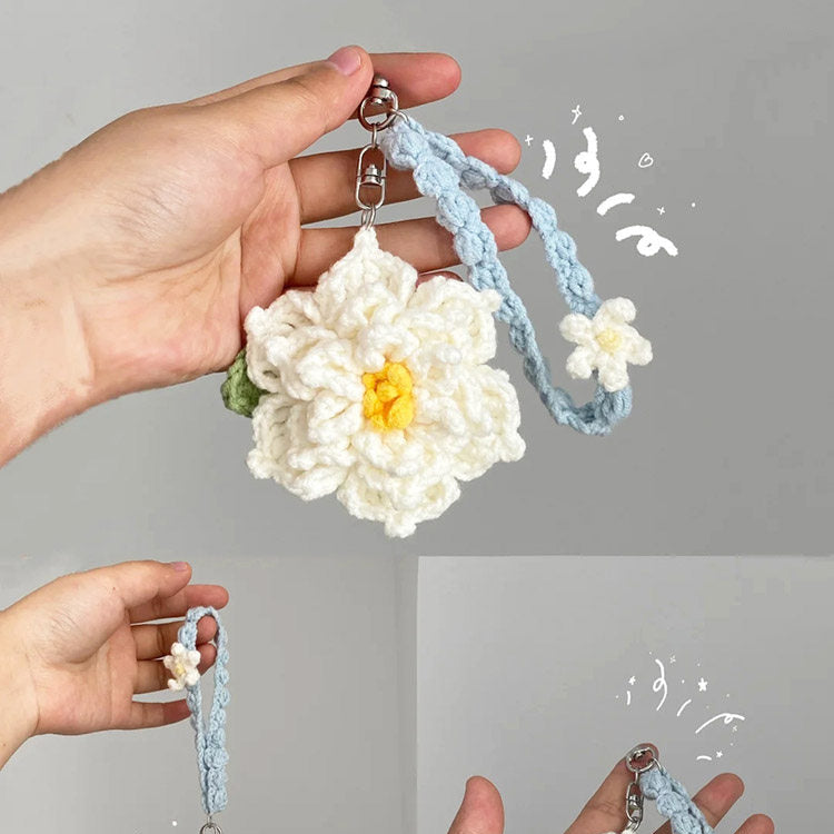 Hand holding a white crocheted flower keychain with a blue strap against a gray background
