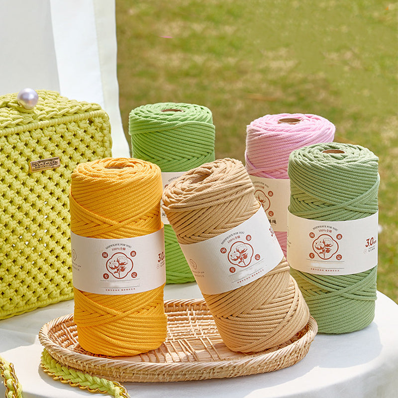Five balls of yarn in yellow, green, and pink on a woven tray with a blurred natural background.