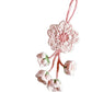 Pink crocheted flower ornament on a gray surface with yarn and a book in the background.