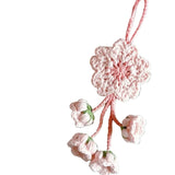 Pink crocheted flower ornament on a gray surface with yarn and a book in the background.