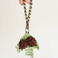 Hand holding a keychain with pine cone design on a plain background