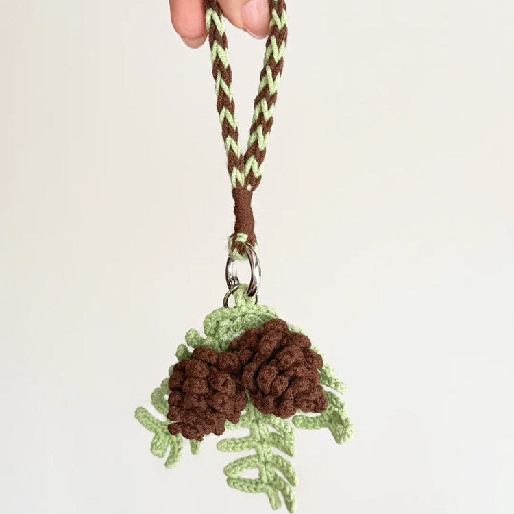 Hand holding a keychain with pine cone design on a plain background