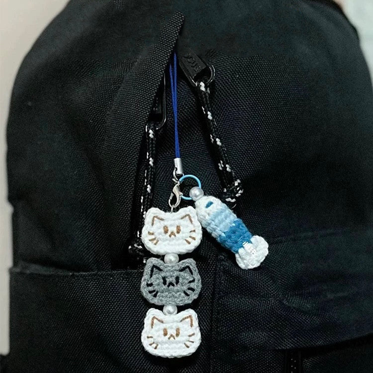 Three cat-shaped keychains hanging from a black bag.