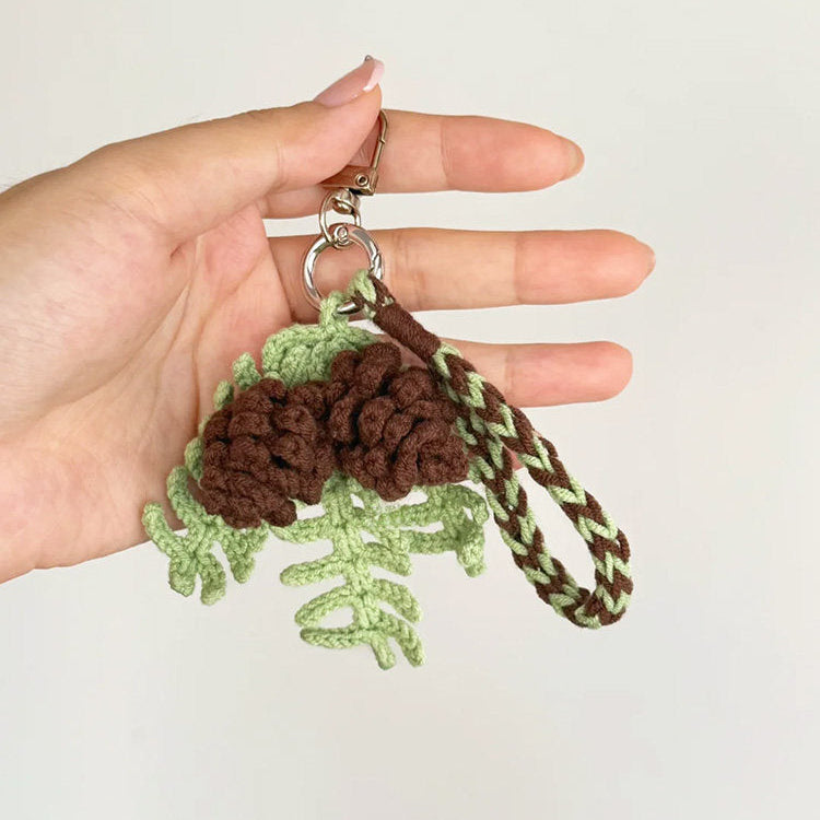 Hand holding a green and brown crocheted keychain against a plain background