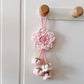 Pink crocheted flower decoration hanging on a white door with wooden hooks.