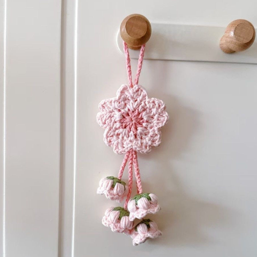 Pink crocheted flower decoration hanging on a white door with wooden hooks.