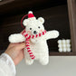 White teddy bear with a red scarf and hat held by a hand against a neutral background