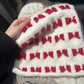 White knitted hat with red patterns held by a hand against a dark background