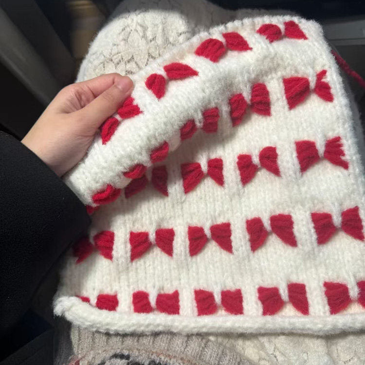 White knitted hat with red patterns held by a hand against a dark background