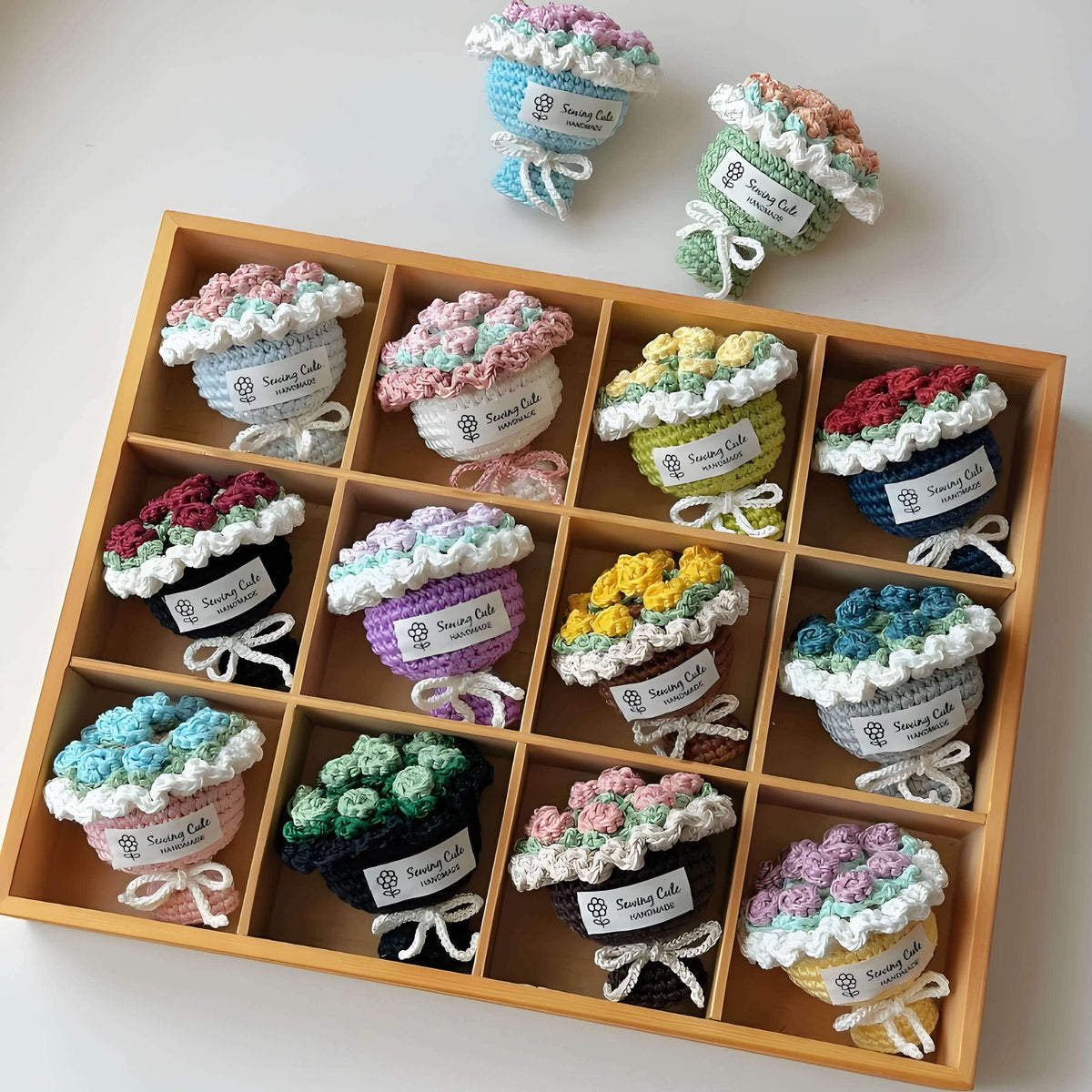 Wooden box with compartments containing small crocheted flower pots on a white background