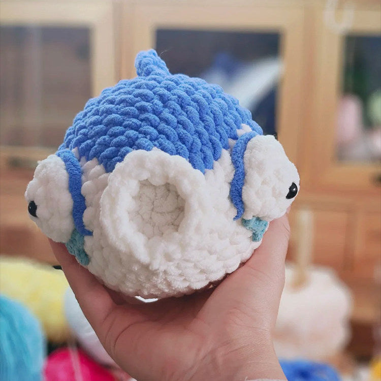 Hand holding a blue and white knitted toy with a blurred background
