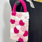 Crocheted pouch with pink and white floral pattern attached to a black bag.