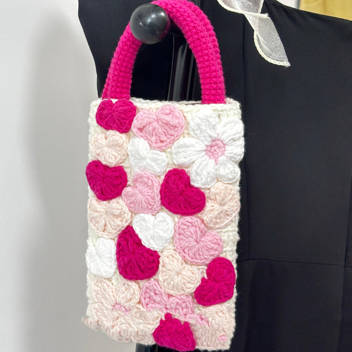 Crocheted pouch with pink and white floral pattern attached to a black bag.