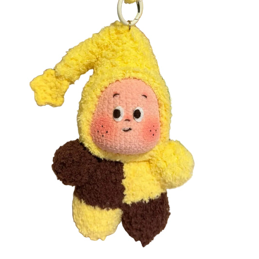 Plush keychain in the shape of a character with a yellow outfit and brown pants on a textured surface.