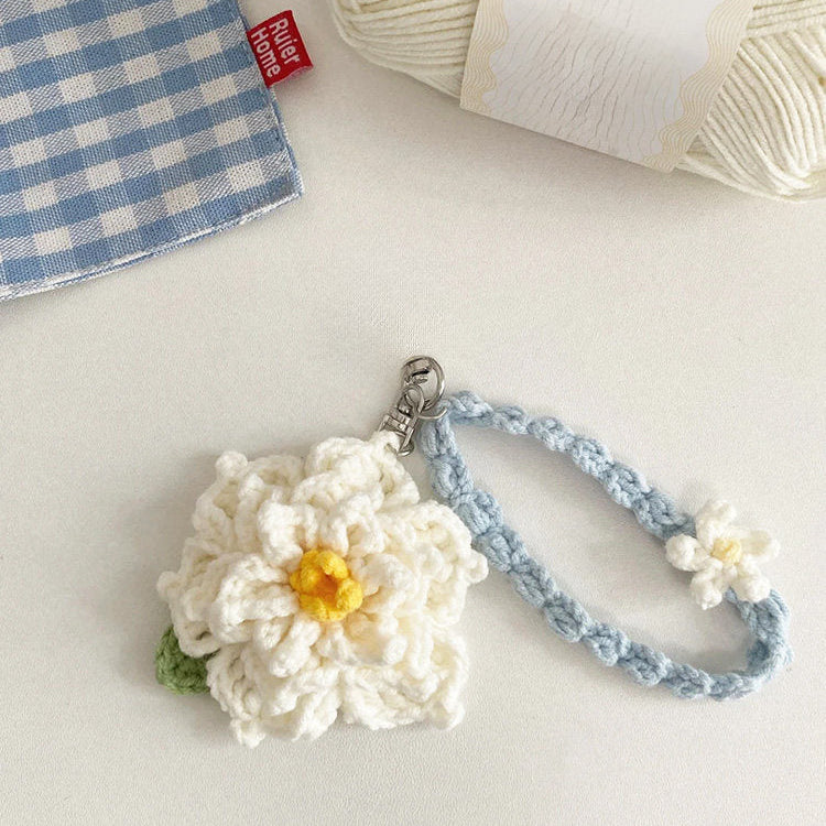 Crocheted flower keychain with a blue strap on a light surface next to yarn and a red label.