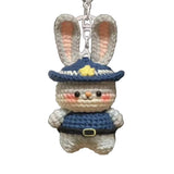 Crocheted rabbit keychain with a blue hat and outfit hanging from a bag.