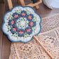 Crocheted mandala mat with a crochet hook and tassel on a textured surface