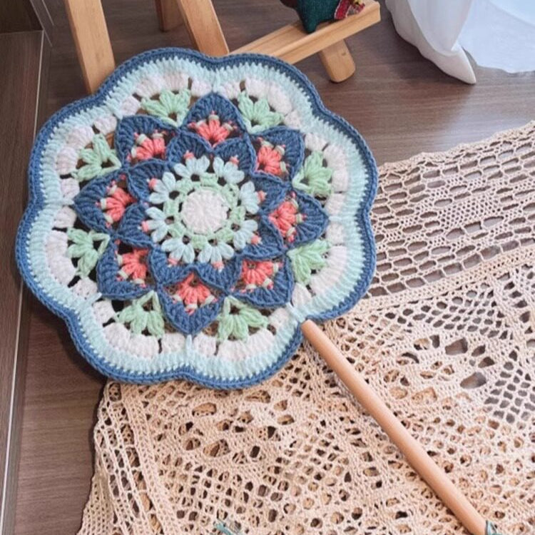 Crocheted mandala mat with a crochet hook and tassel on a textured surface