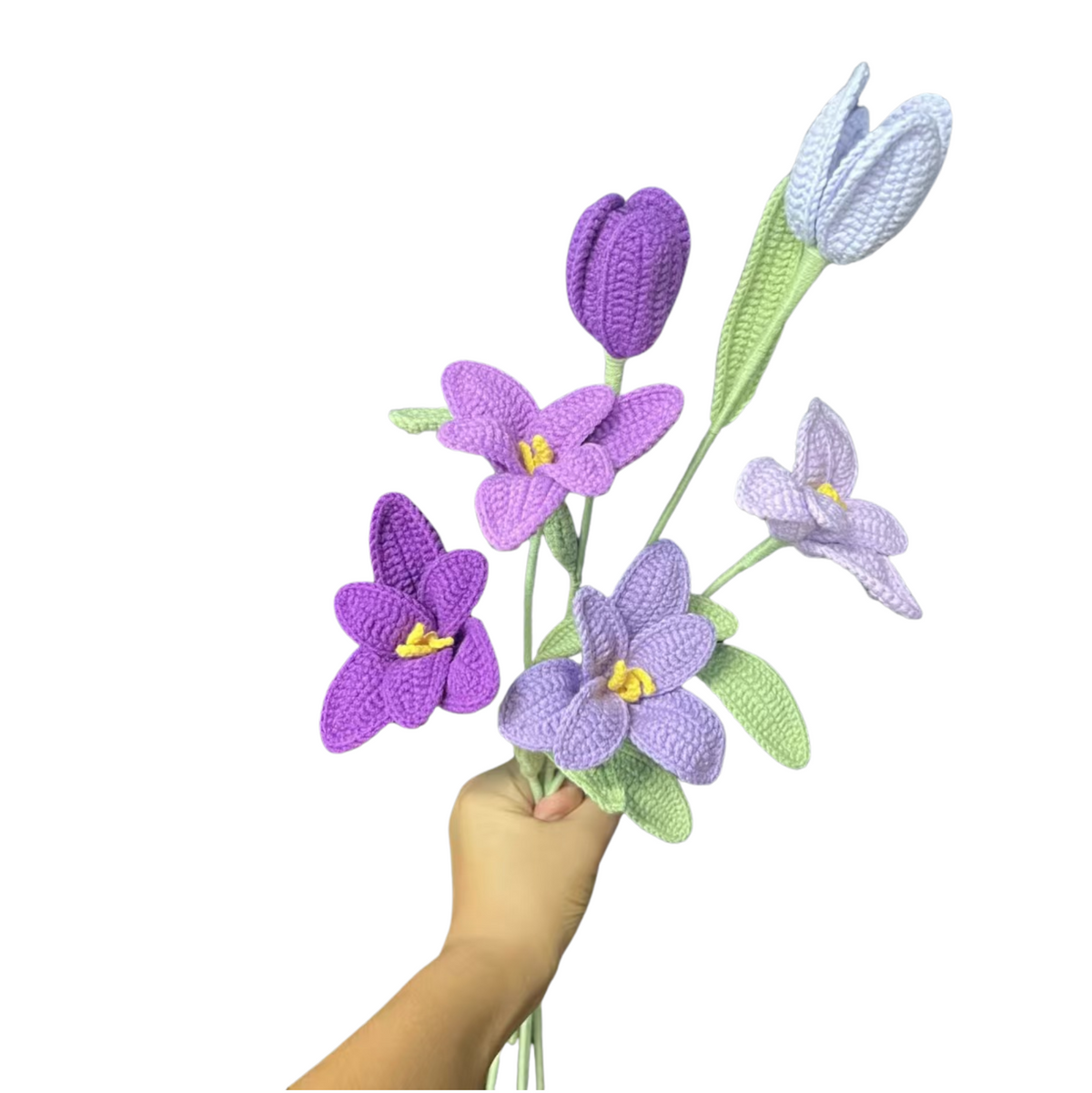 Hand holding a bouquet of crocheted purple and green flowers on a white background