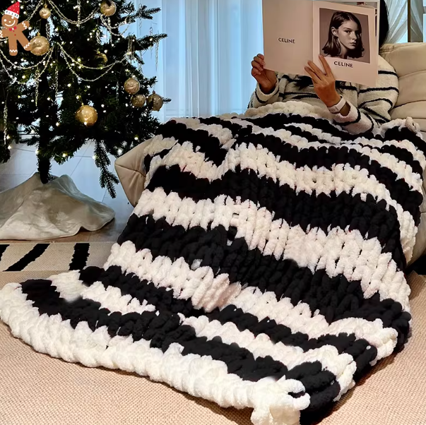 Person sitting on a couch under a black and white striped blanket with a Christmas tree in the background.