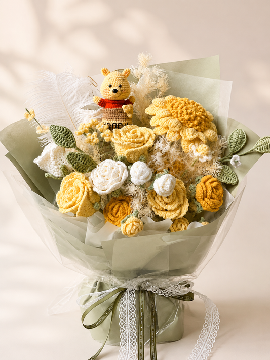 Handmade crochet flower bouquet featuring yellow and white flowers, green leaves, a small Winnie the Pooh bear figure, and soft white feathers, wrapped in pale green tissue paper with a ribbon bow.