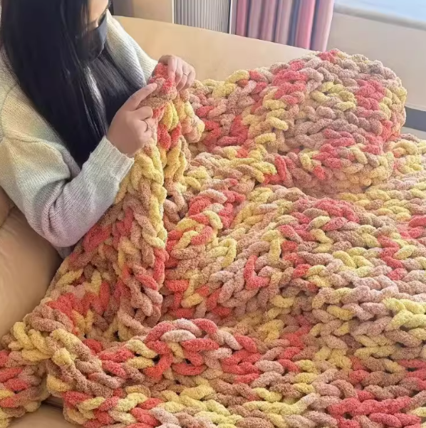 Person holding a colorful knitted blanket with pink, yellow, and beige tones.