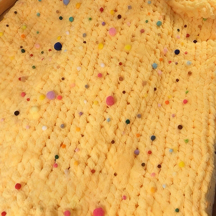 Person holding a phone over a yellow textured blanket with colorful dots, wearing a white robe.
