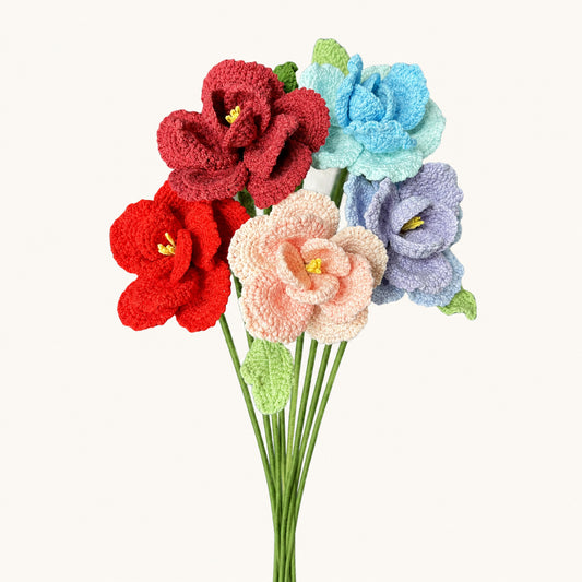 A bouquet of six crocheted fabric flowers in red, light blue, lavender, and pale pink, with green stems and leaves, set against a plain off-white background.