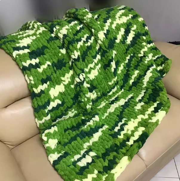 Green and white crocheted blanket draped over a beige couch.