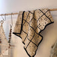 Crocheted blanket with black trim hanging on a wooden rack against a neutral wall.