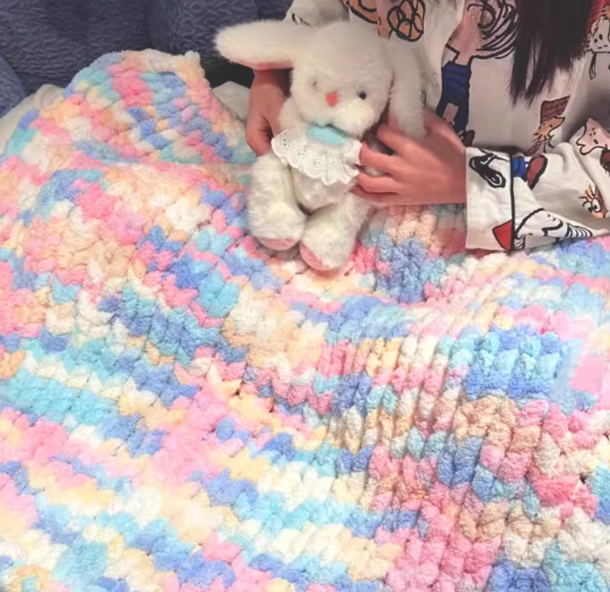 Person holding a plush toy on a colorful crocheted blanket
