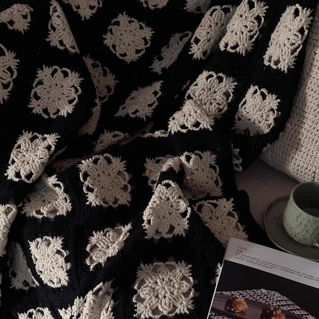 Black and white crocheted blanket with a pattern, next to a book on a surface.