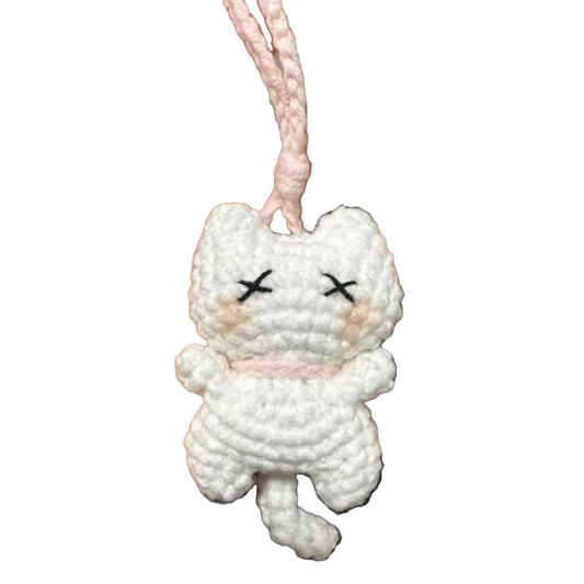 White crocheted cat charm held in a hand against a blurred background