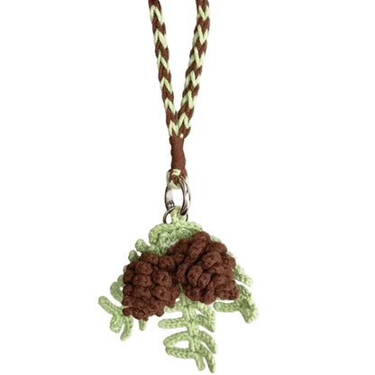 Hand holding a keychain with pine cone design on a plain background