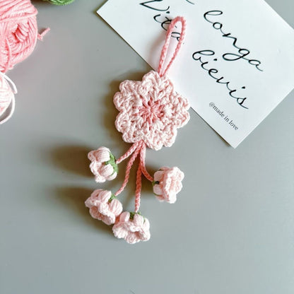 Pink crocheted flower ornament on a gray surface with a card in the background.