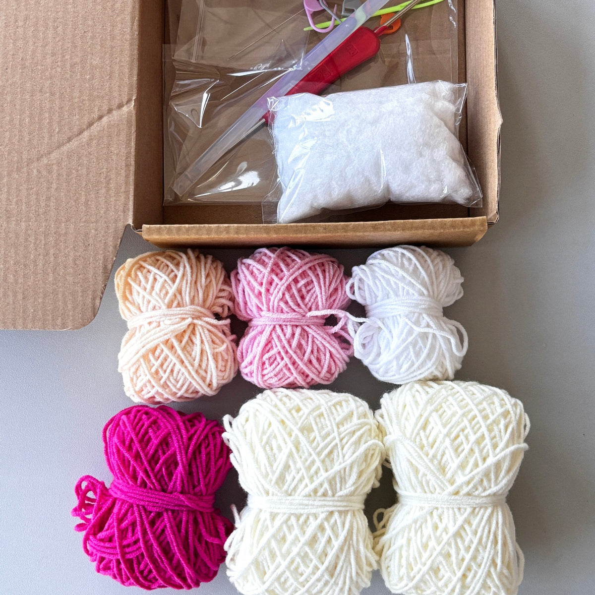 Yarn balls in various colors with a cardboard box containing knitting tools on a light background