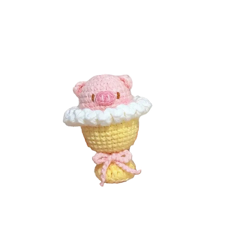 Hand holding a small crocheted cupcake with pink frosting and a bow, with yarn balls in the background.