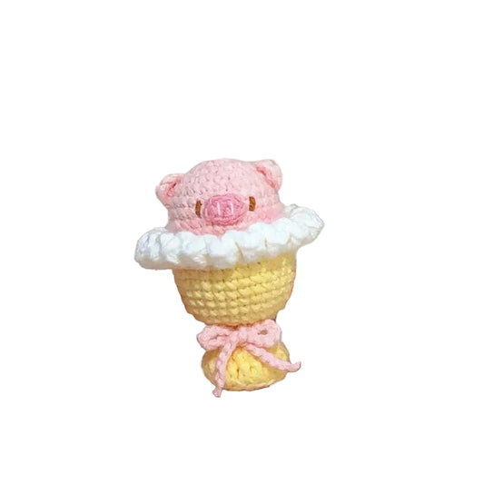 Hand holding a small crocheted cupcake with pink frosting and a bow, with yarn balls in the background.