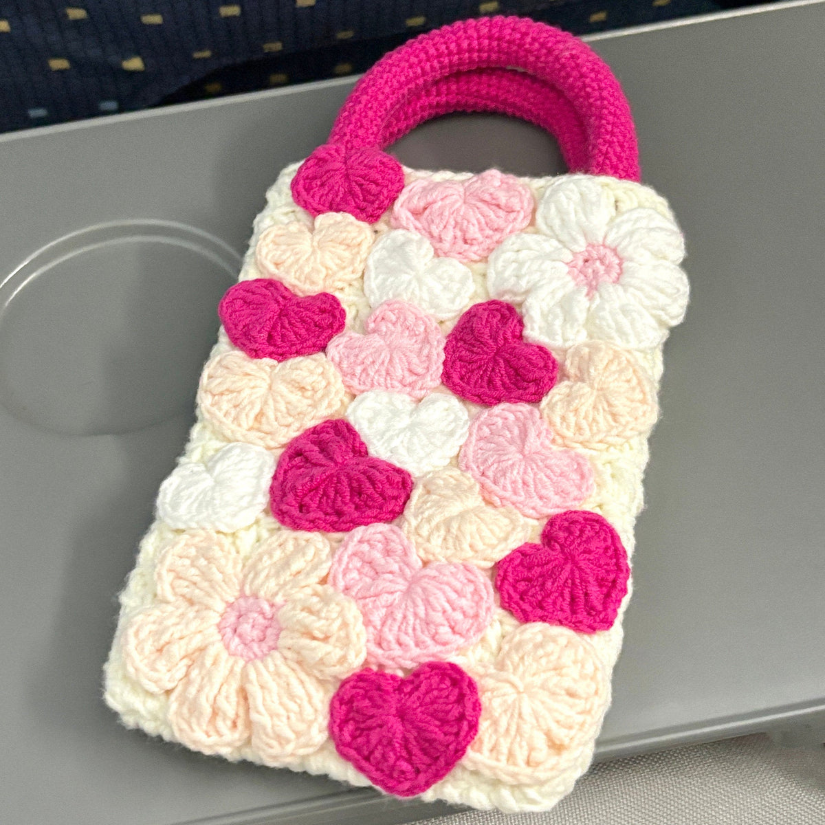 Crocheted bag with pink and white floral pattern on a gray surface