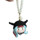 Crocheted character keychain with pearl necklace against a blurred background of figurines