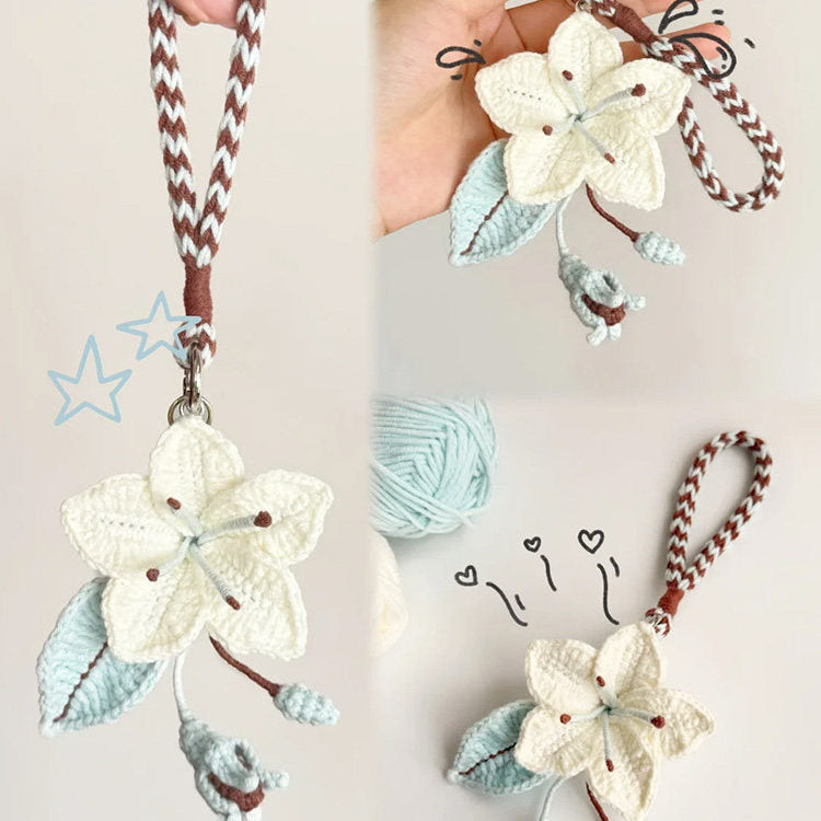 Handmade crochet flower keychain held by a hand with yarn ball and hooks in the background.