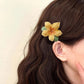 Person wearing a yellow flower hair clip on wavy hair against a neutral background
