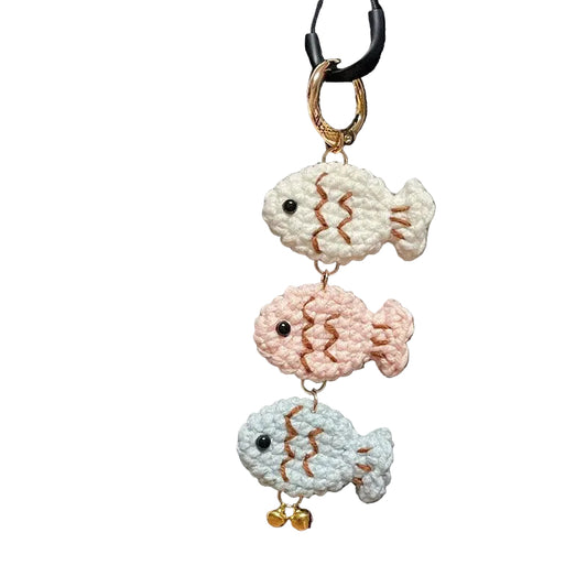 Three crocheted fish keychains on a black bag with visible branding.