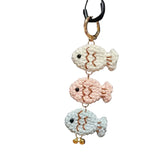 Three crocheted fish keychains on a black bag with visible branding.