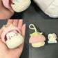 Small crocheted toy resembling a cat in a pink hat next to a ball of white yarn on a dark surface.